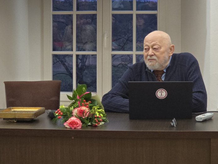 Prof. ALeksander Naumow za stołem, obok leży bukiet kwiatów