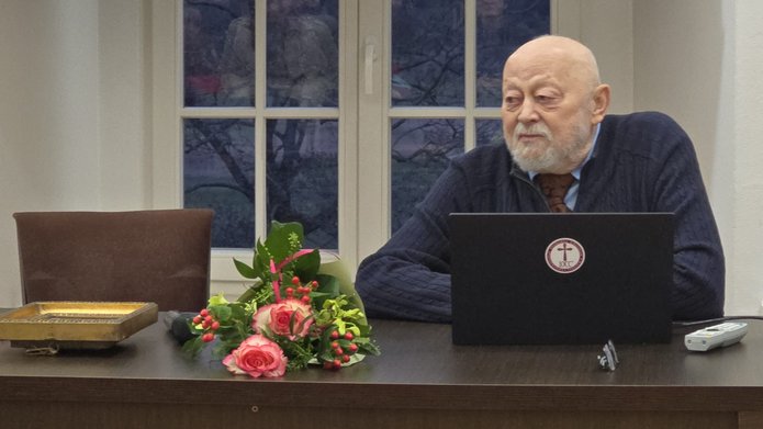 Prof. ALeksander Naumow za stołem, obok leży bukiet kwiatów